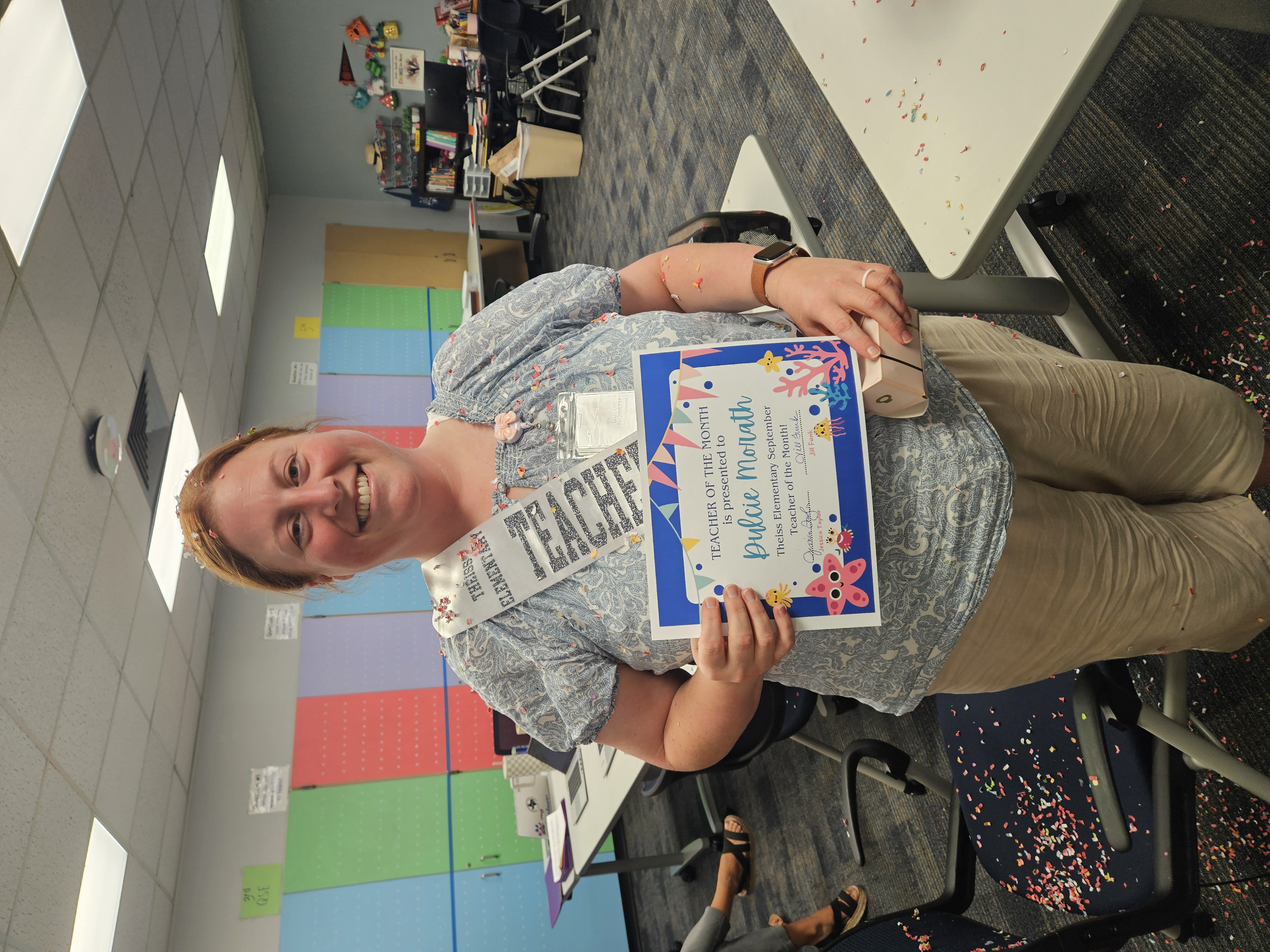 teacher smiling with a certificate for Teacher of the MOnth