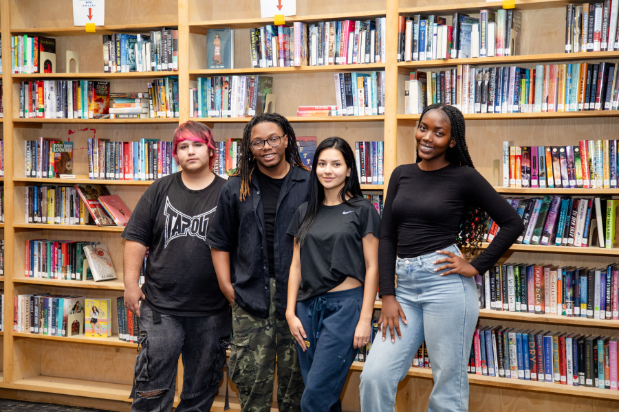 NEC students smiling in front of the bookcase.