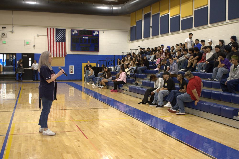 NEC principal speaking to students sitting in bleachers at the gym