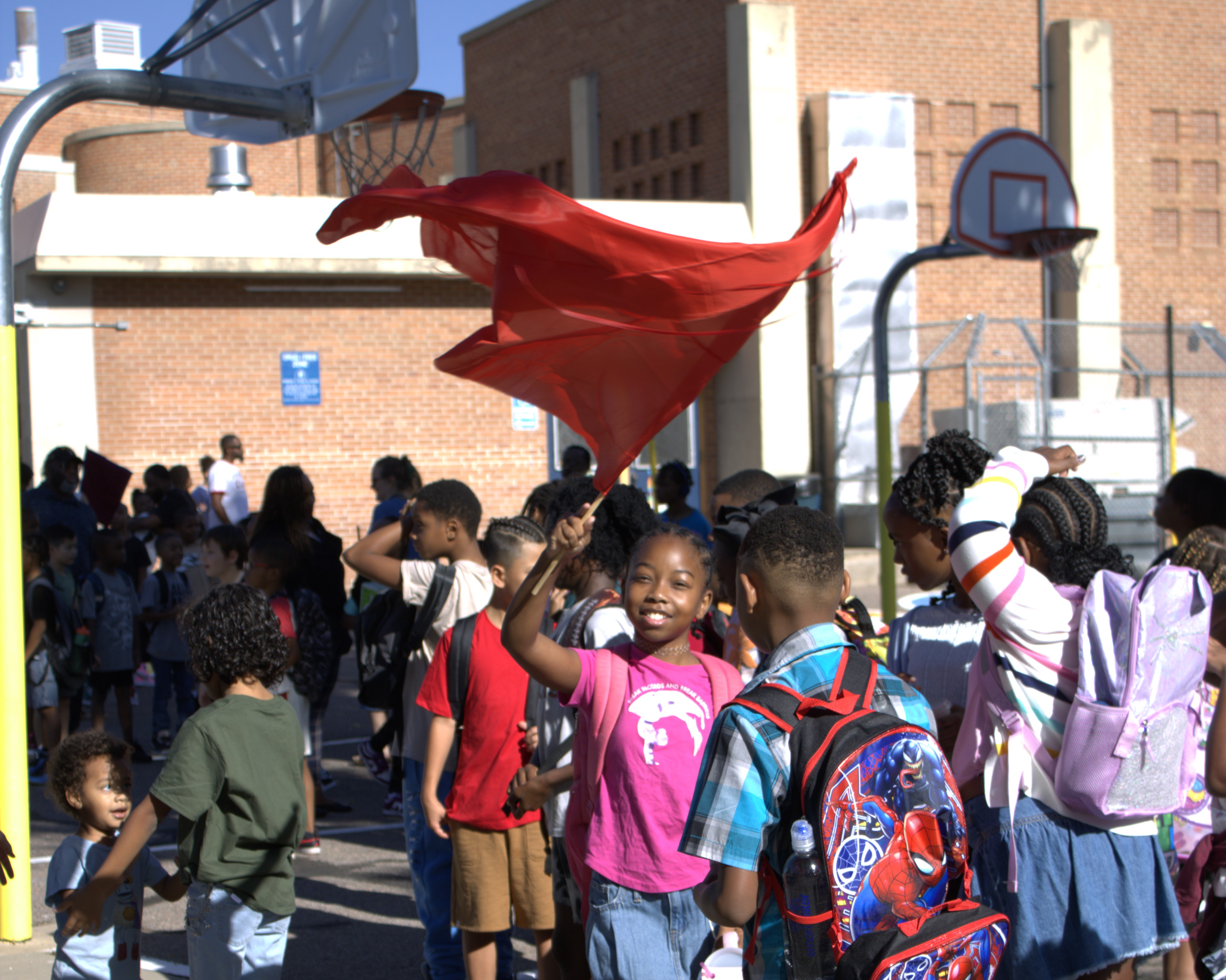 Hallett student waving a flag and smiling in a sea of classmates outside.