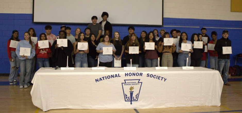 Students hold up their NHS certificates in front of a table with candles and "national honor society" printed on the tablecloth.