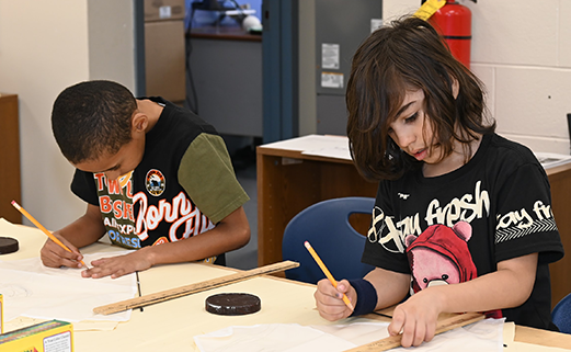 Two students working at table with pencils in hand