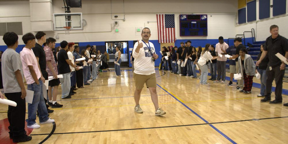 NEC staff member walking in the gym holding a thumbs up and smiling while two lines of students stand on either side of him