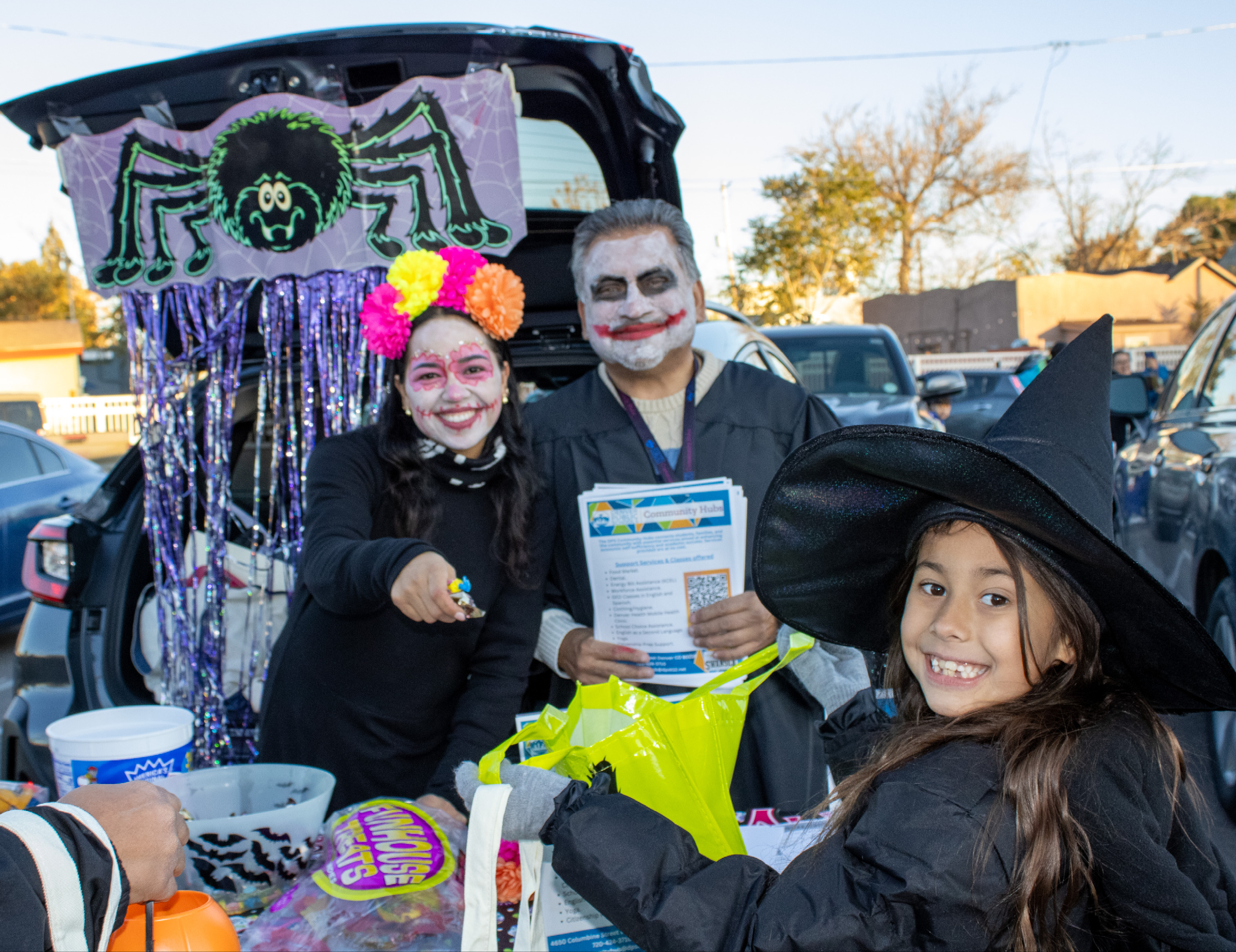 A student smiles for a photo and holds her bag out for candy at Trunk or Treat