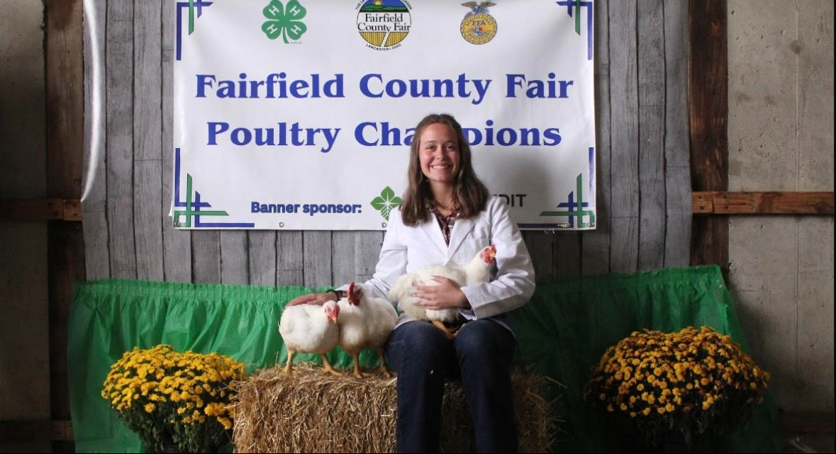 Makenna Lybarger sits on a hay bale with three chickens.