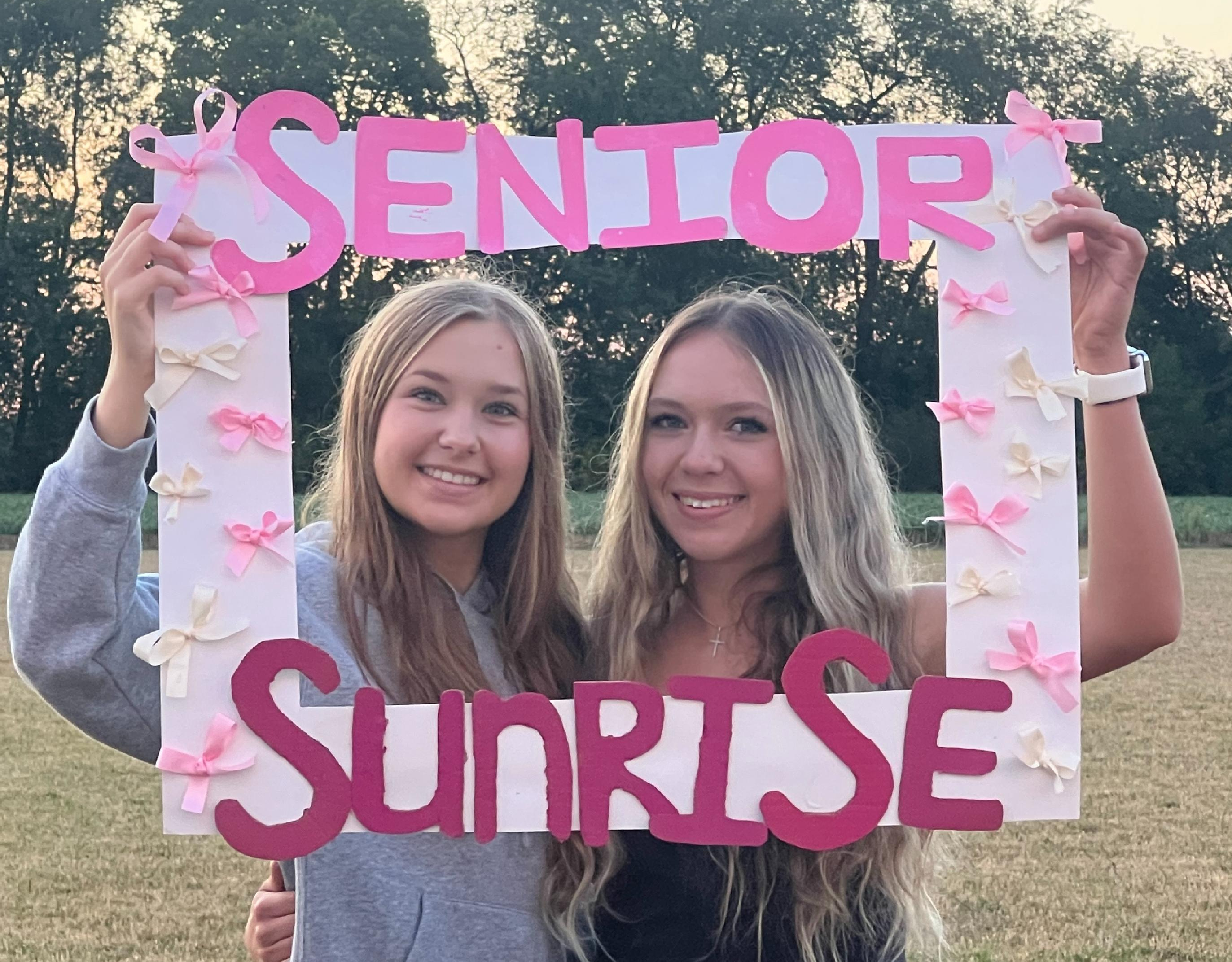 Two female students holding up a frame reading "Senior Sunrise"