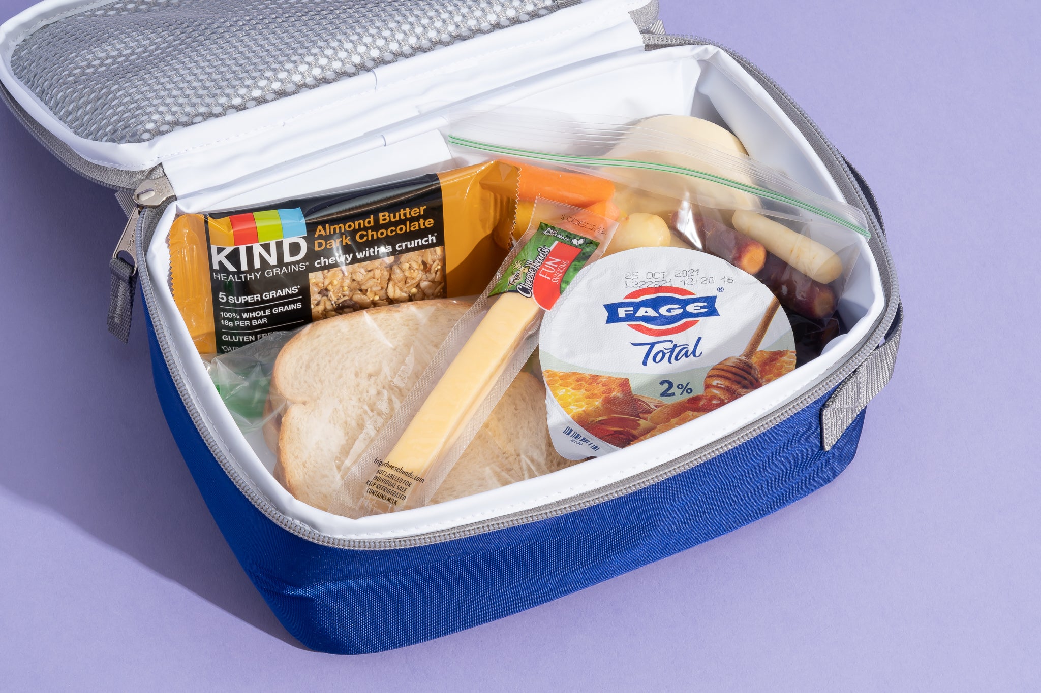 An open lunch box with sandwich, granola bar, cheese stick, and yogurt inside