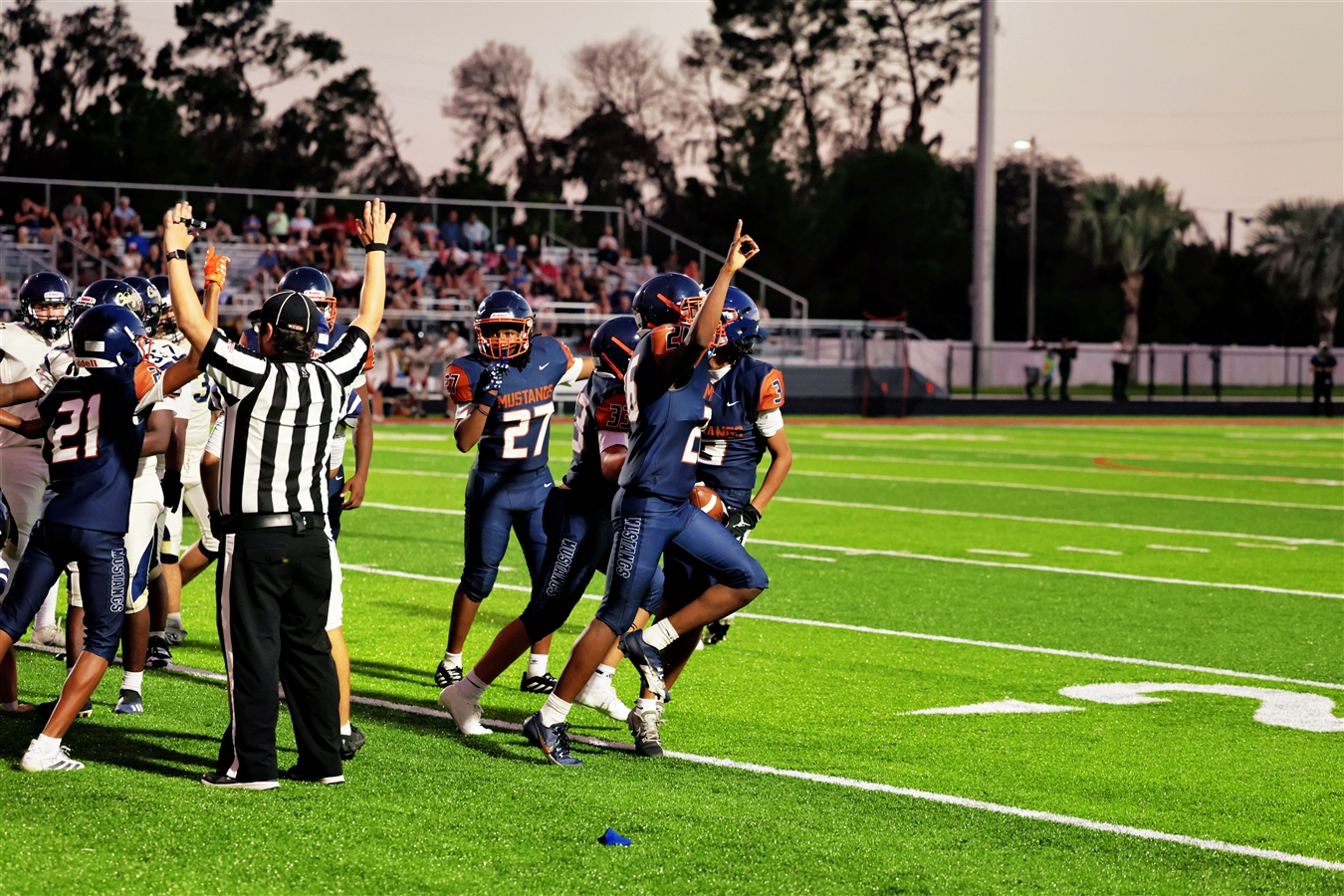 football players celebrating after a touchdown. referee has his hands up for a touchdown complete