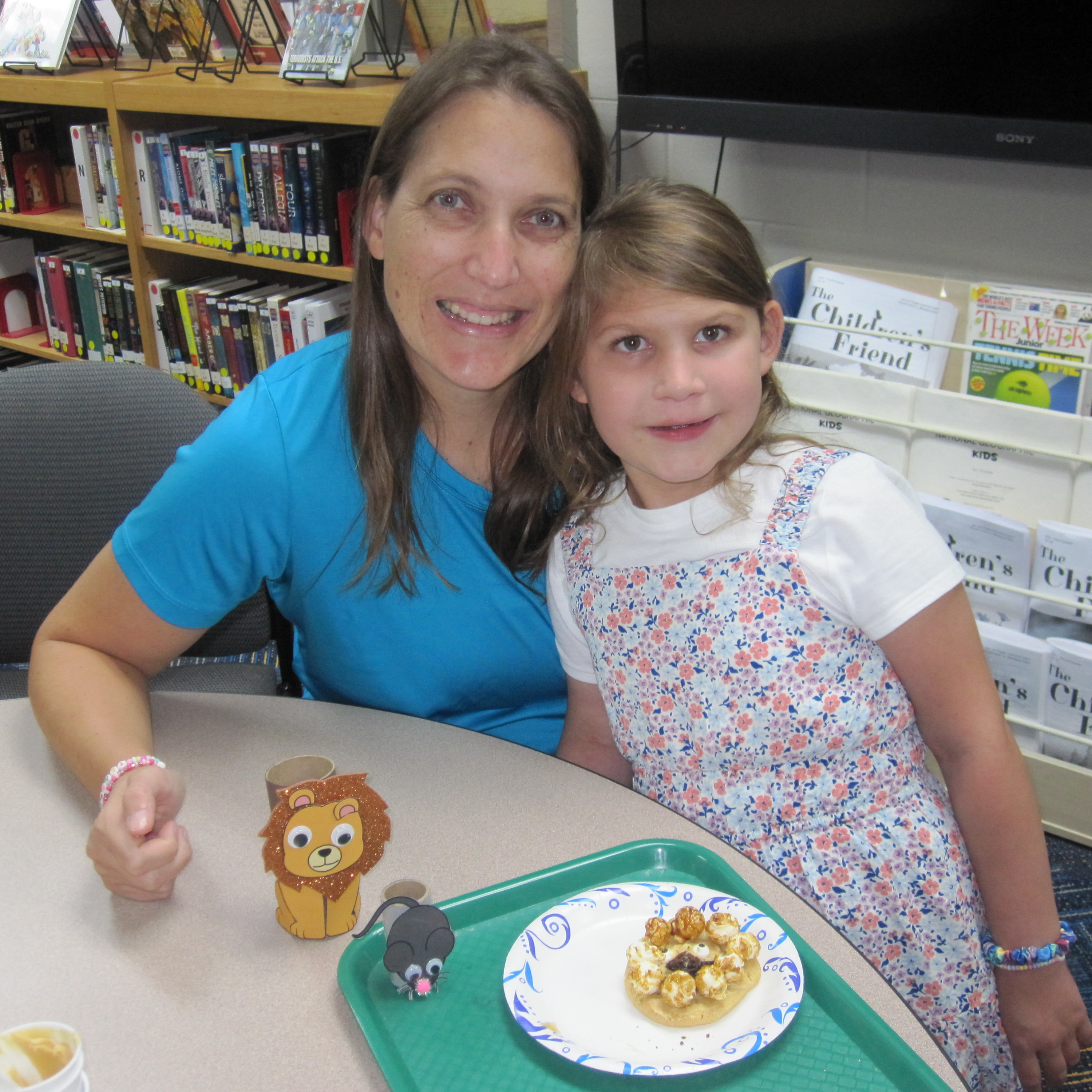 Ellie and her mother smiling with Ellie's cookie creation and the papercraft animals on the table