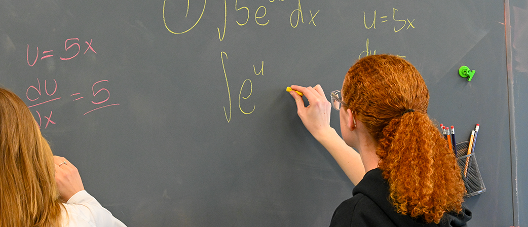 Two students working on algebra equations on a chalboard