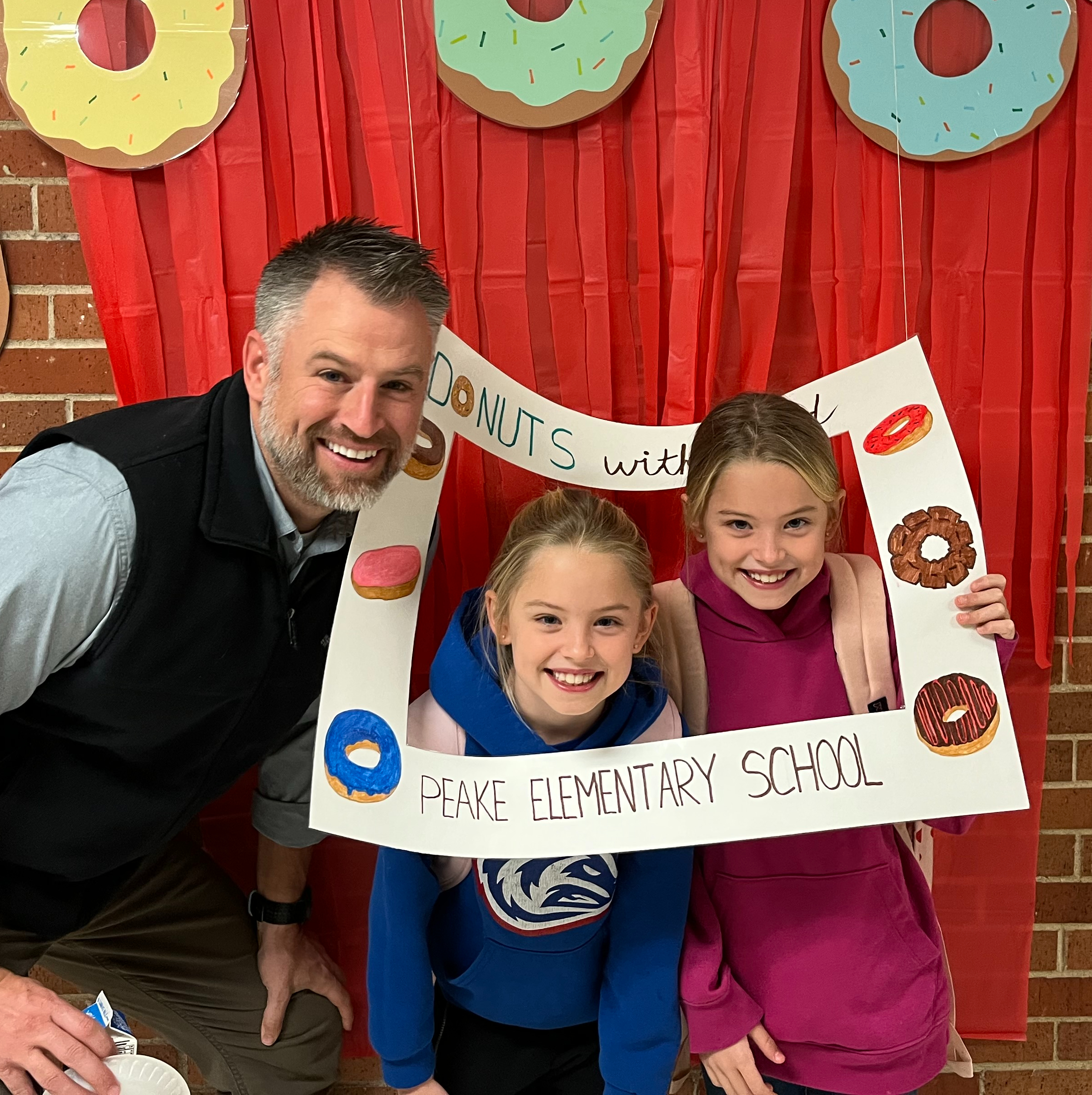 children and dad smiling in a picture frame that says "donuts with Dads"