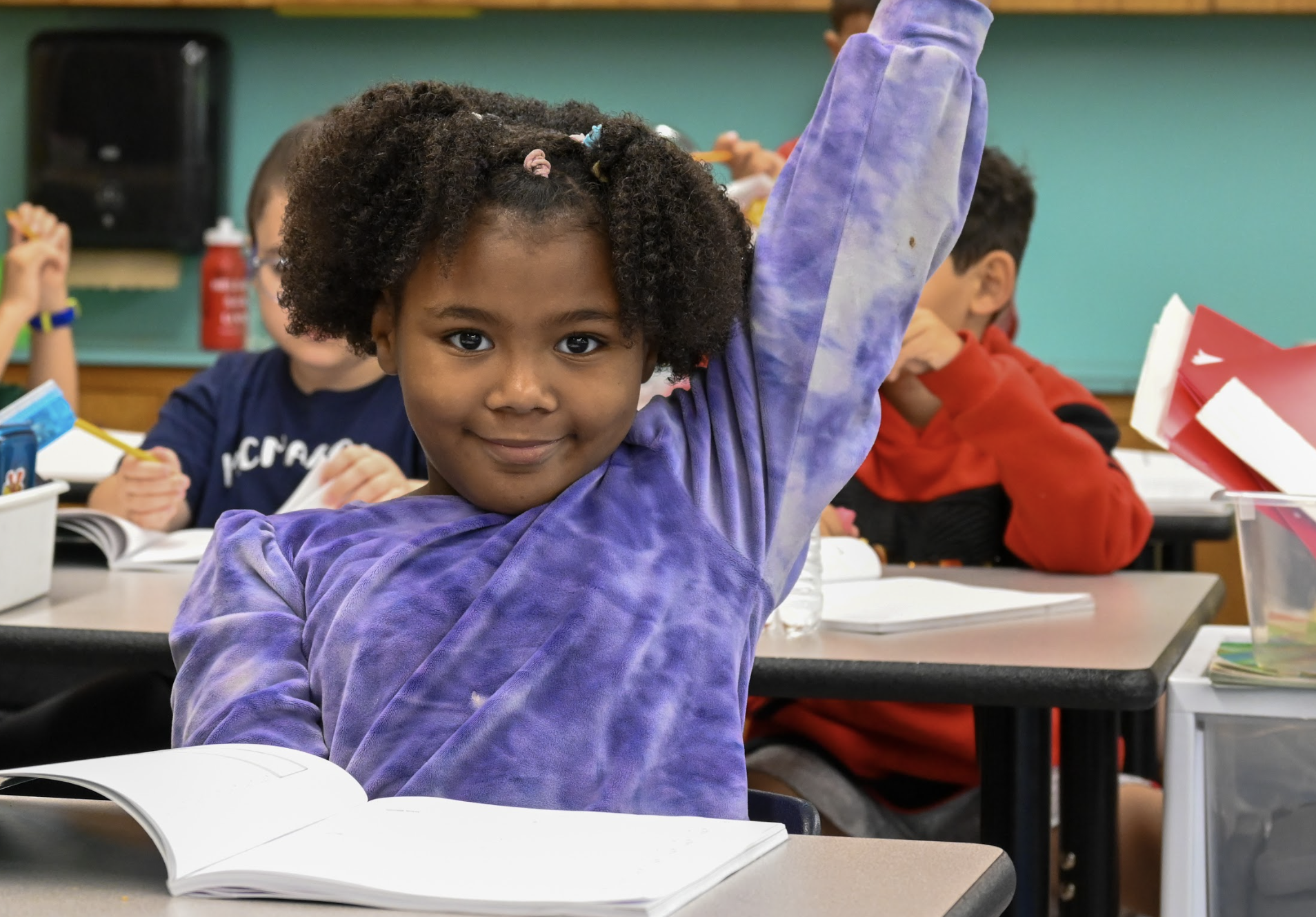 Student raises her hand with a workbook in front of her