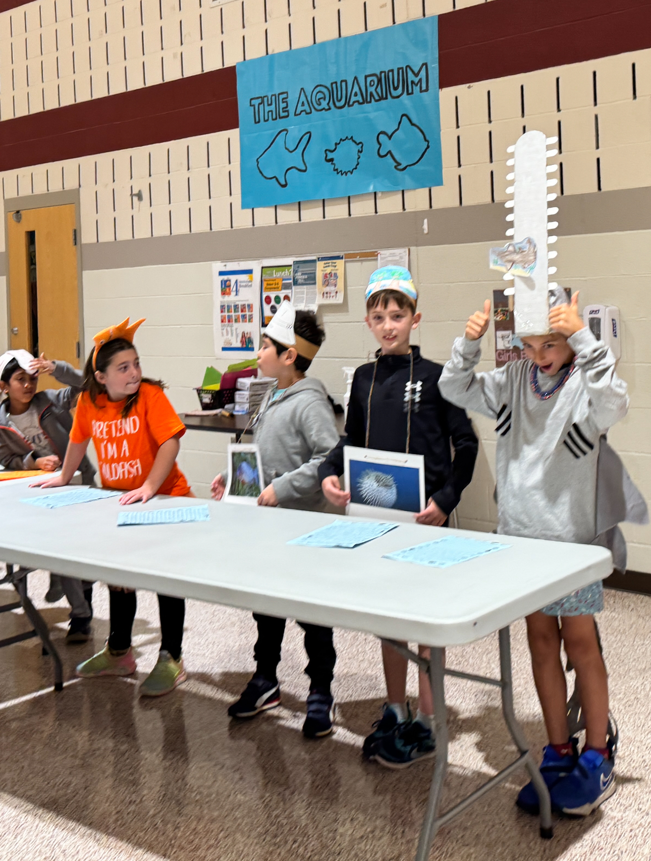 Elementary students standing at a table with "The Aqaurium" sign in back.