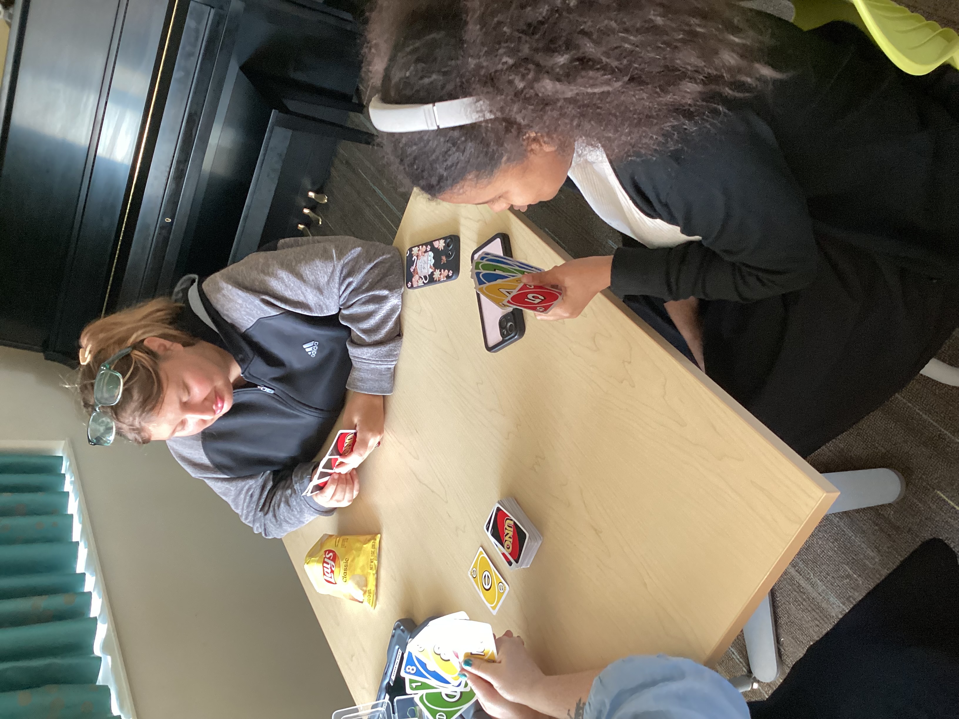 3 students sitting at a table playing Uno; a piano is in the background