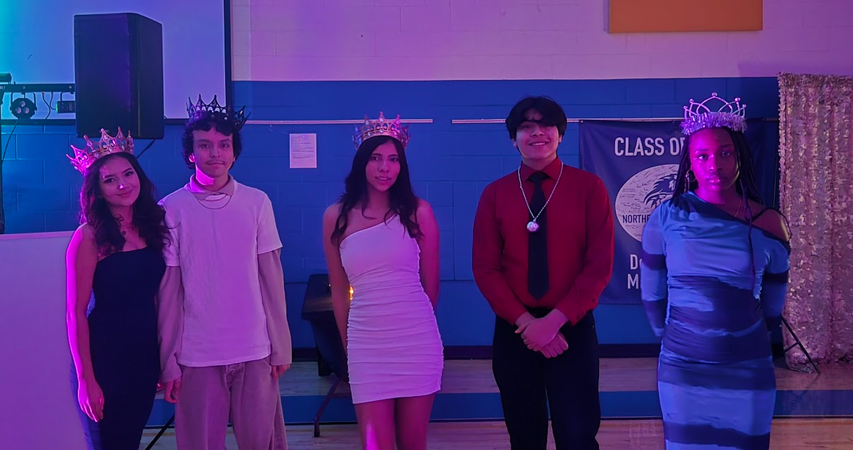 5 students posing in their homecoming outfits in the gym. 4 wearing crowns.
