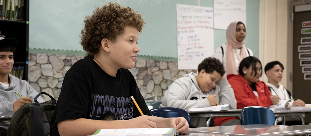 Boy with pencil and textbook in foreground, other students in background