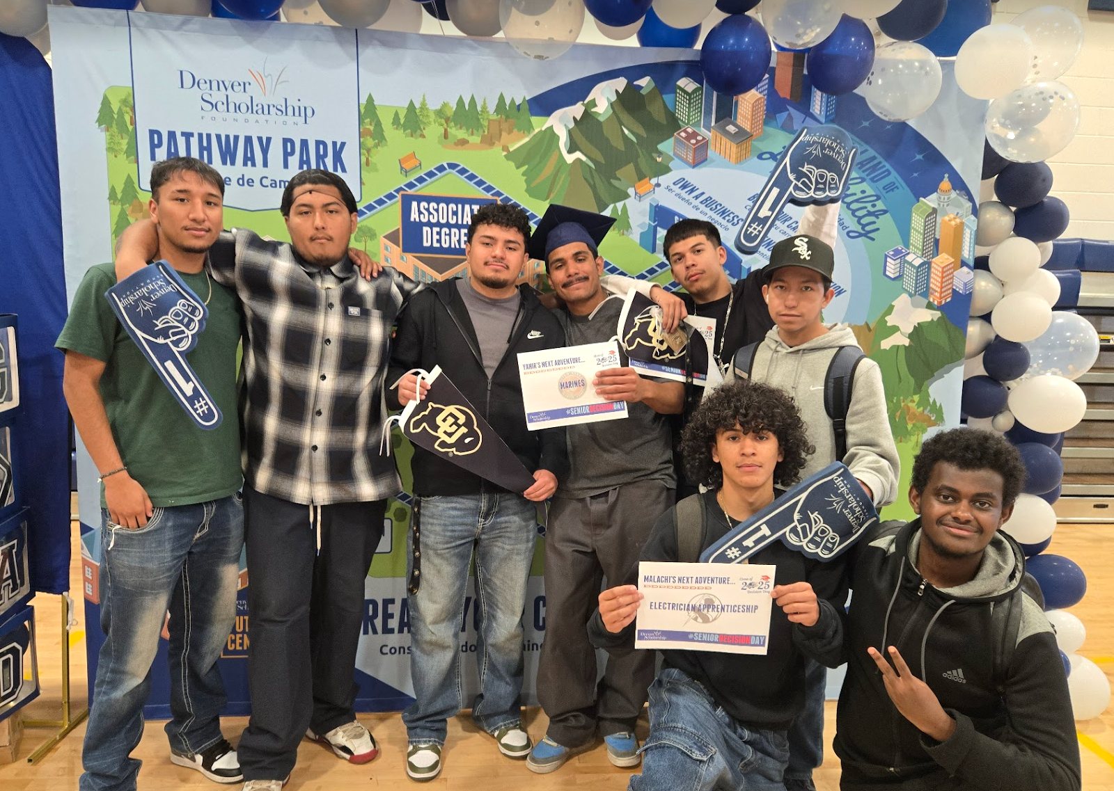 8 students smiling and holding college memorabilia and certificates