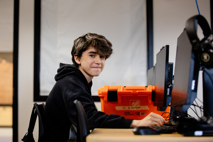 Student sits at computer and smiles at the camera.