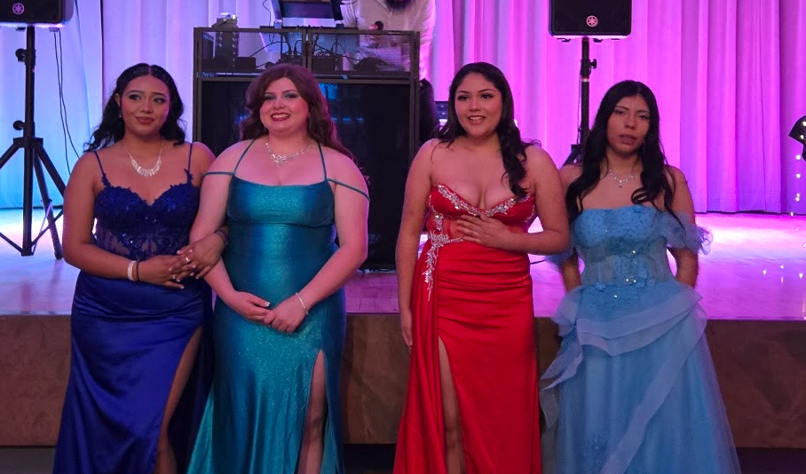 4 students in their prom outfits standing in front of the stage