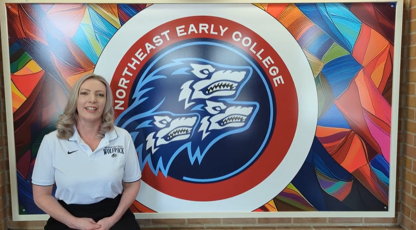 Principal Warren sitting next to NEC's logo mural
