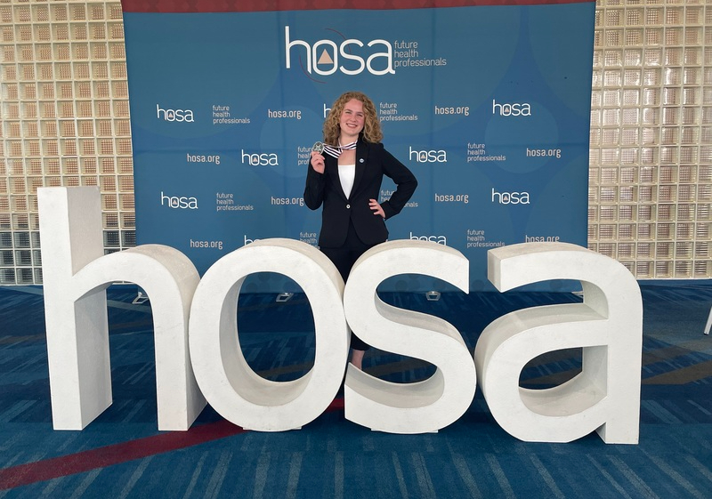 Ella King poses in front of a HOSA decoration