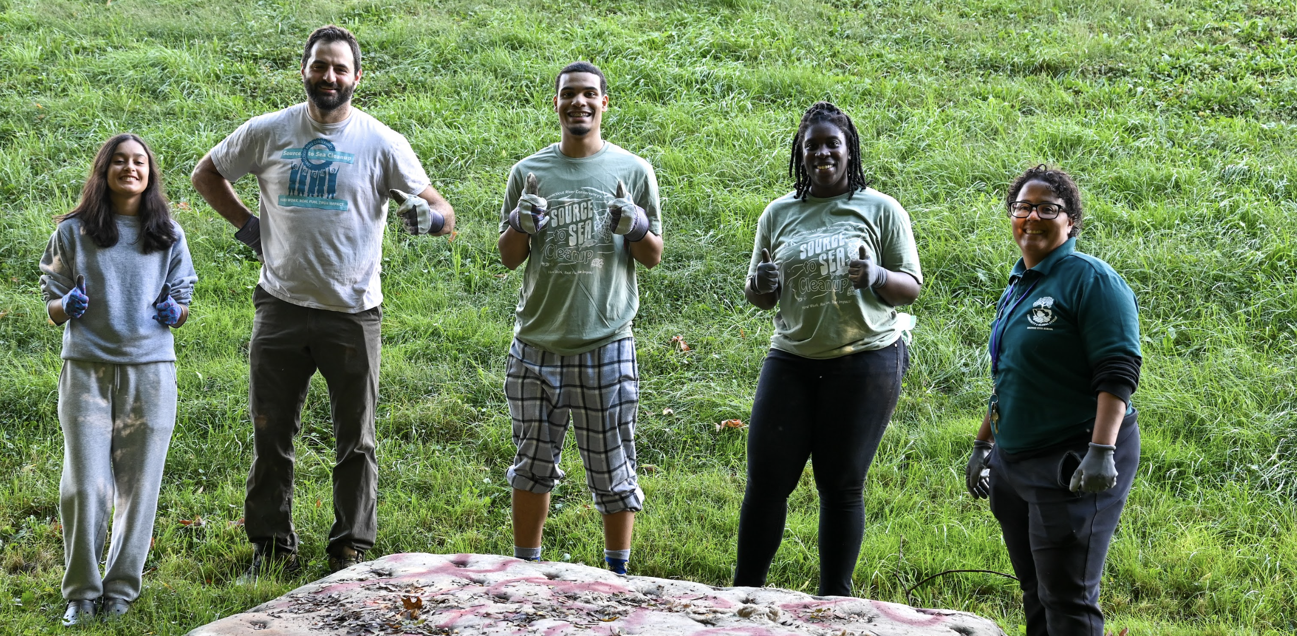 Staff and students stand in front of mattress they removed from the riverbank