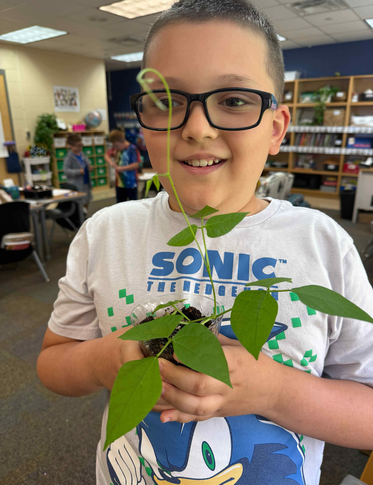 Lukas smiling while holding a plant. He is wearing glasses and has a Sonic the Hedgehog T-shirt on