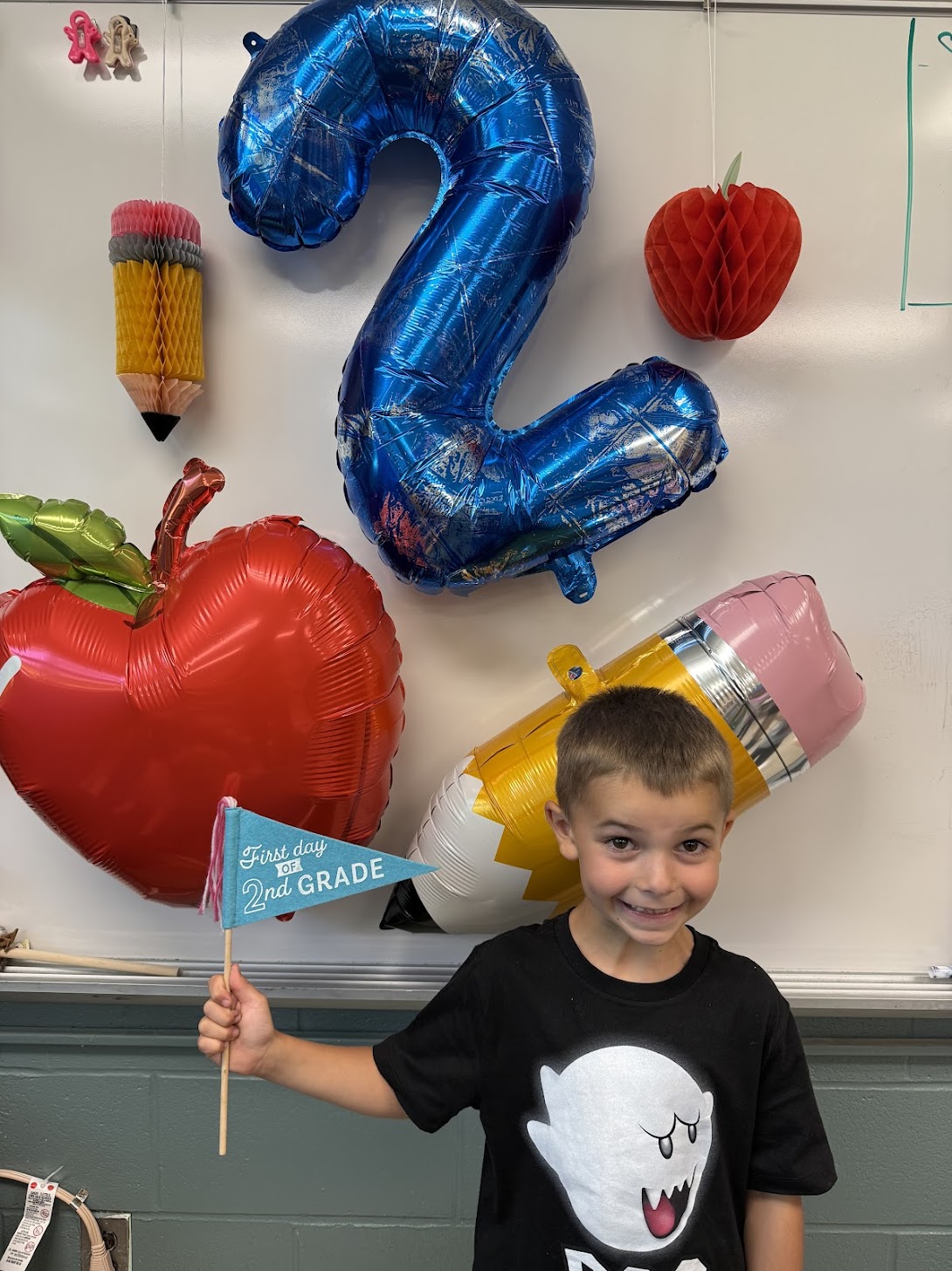 second grade student standing in front of balloons and holding a first day of 2nd grade sign