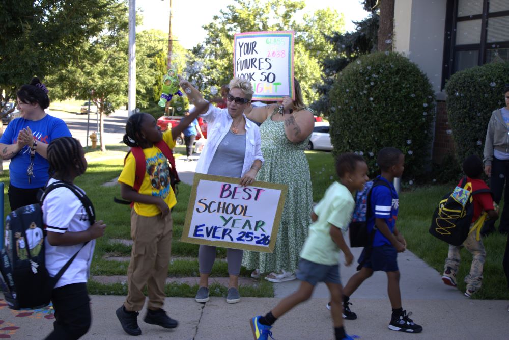Hallett students walking into school as parents and teachers hold up encouraging 1st day of school signs and bubbles