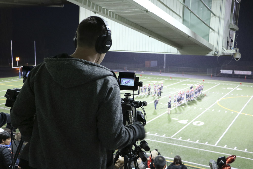 A high school student operates a video camera during a football game