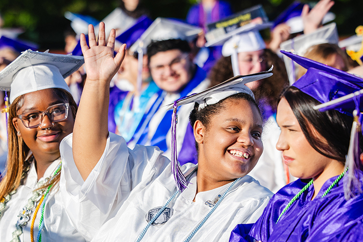 Student waves while wearing graduation cap and gown