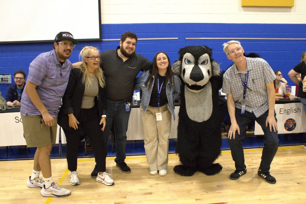 Group teachers smiling and posing with Wolfie mascot in the gym