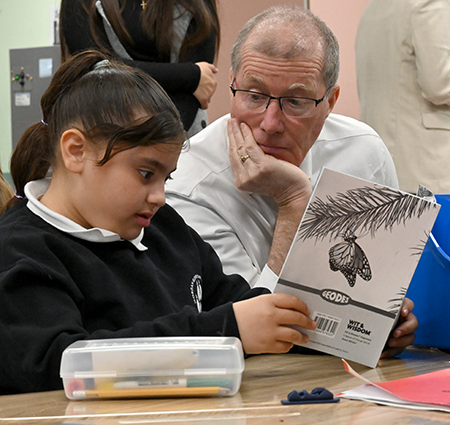 Student reading book as Assistant Superintendent Stephen Mahoney looks on.