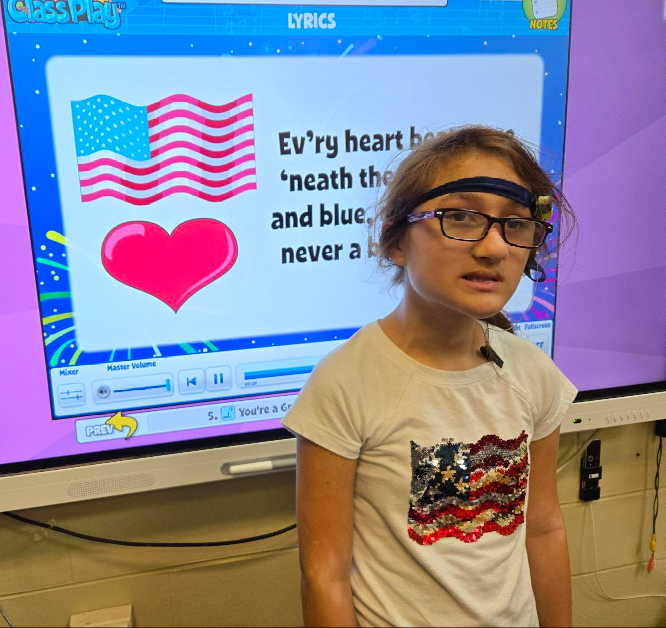 Brianna is wearing an American Flag shirt in front of a board showing lyrics for "You're a Grand Old Flag".