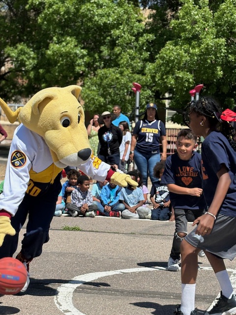 Rocky, the Denver Nuggets mascot, dribbles a basketball on the court with two students.