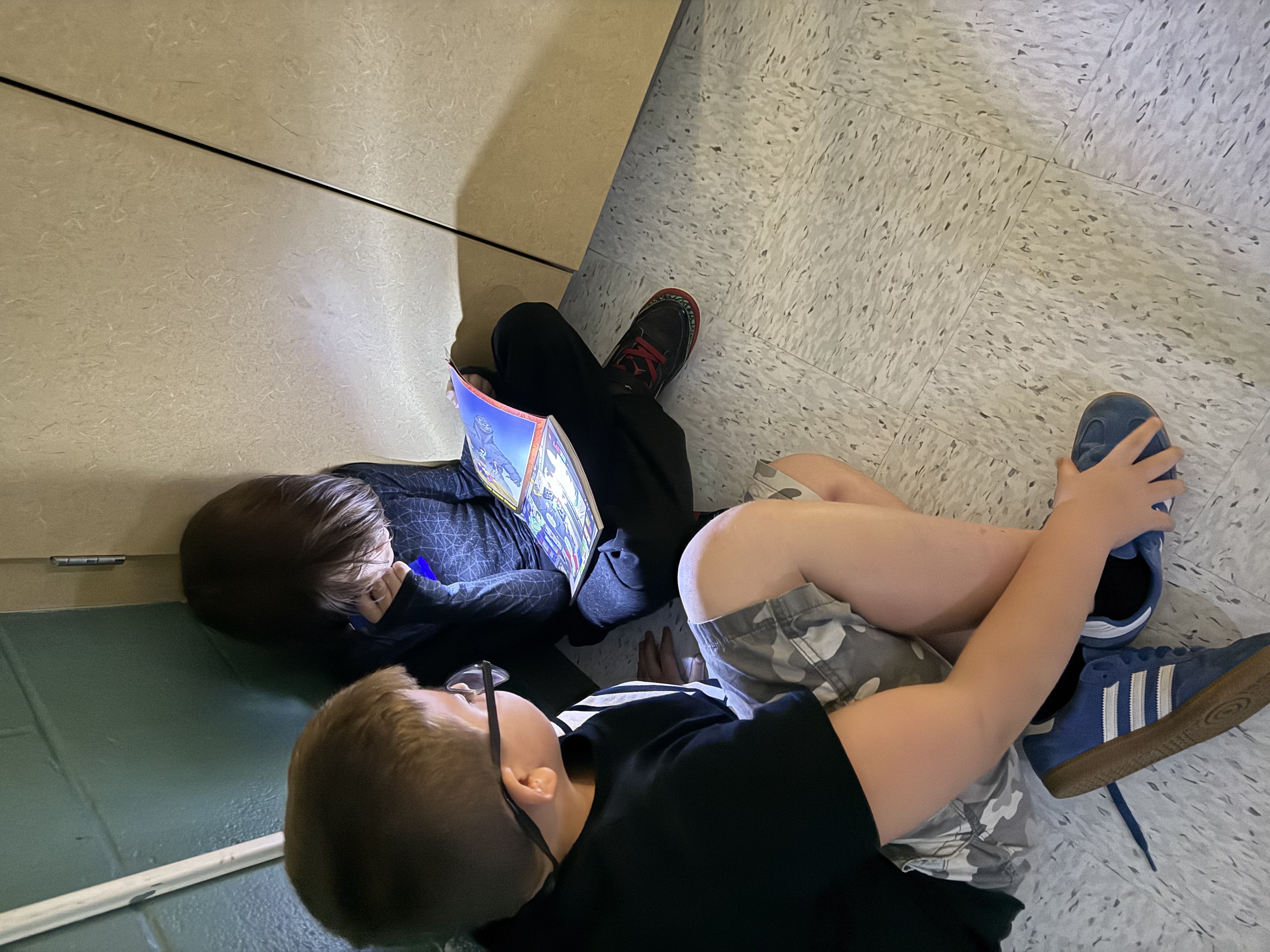 Two boths share reading a book in a cozy corner with a flashlight