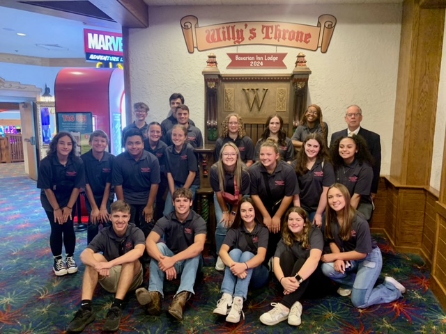 Youth ambassadors sitting and standing in front of Willy's Throne inside the Bavarian Inn Lodge arcade with Randy Hegenaur