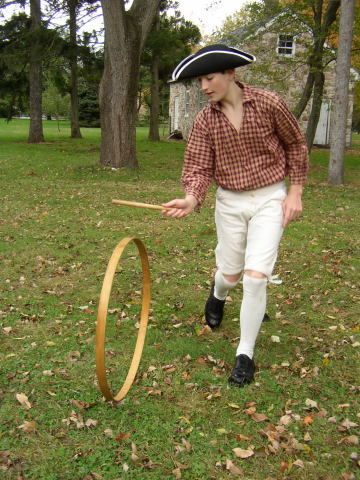 boy in colonial dress rolling a wooden hoop