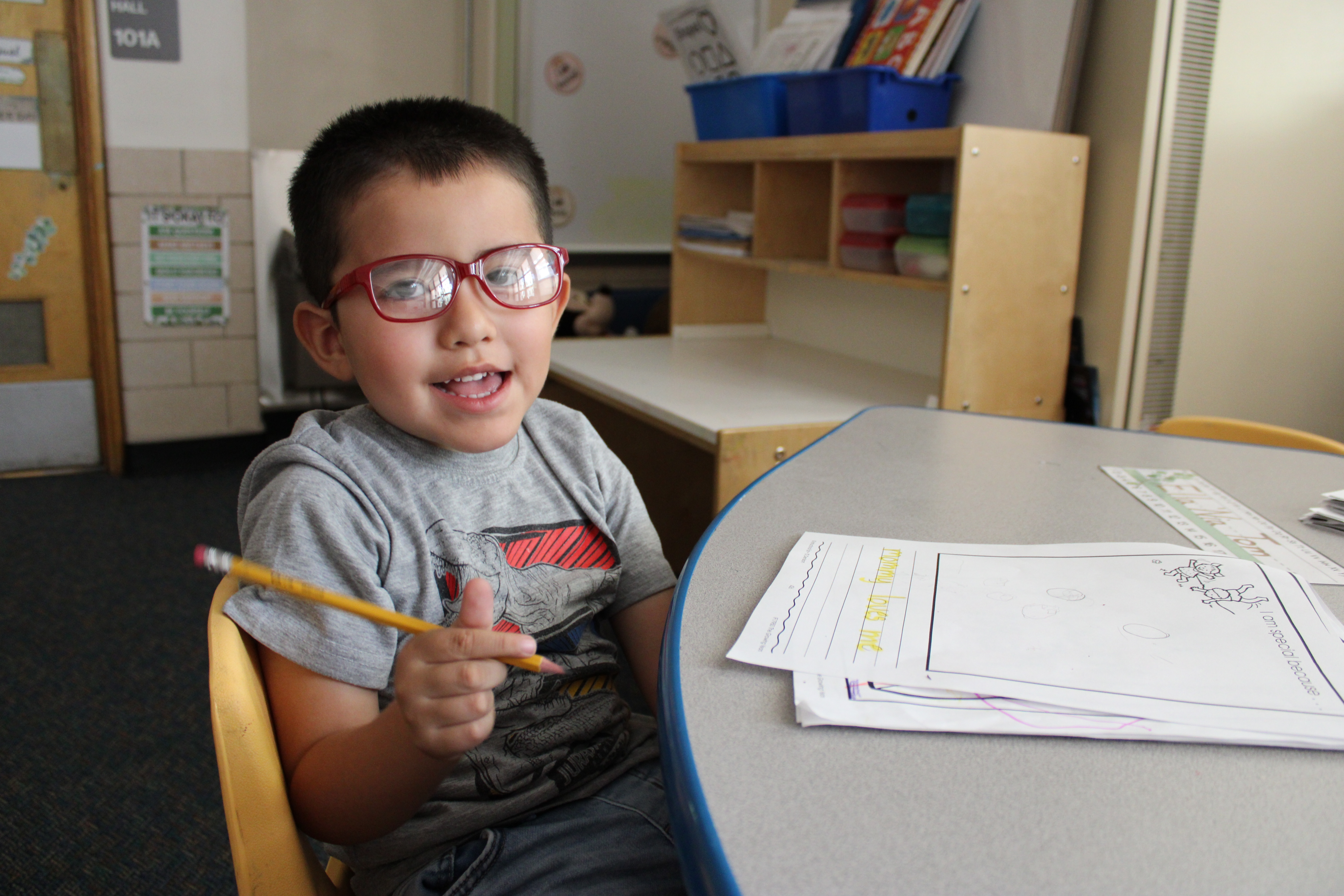 student smiling at his desk with his toys